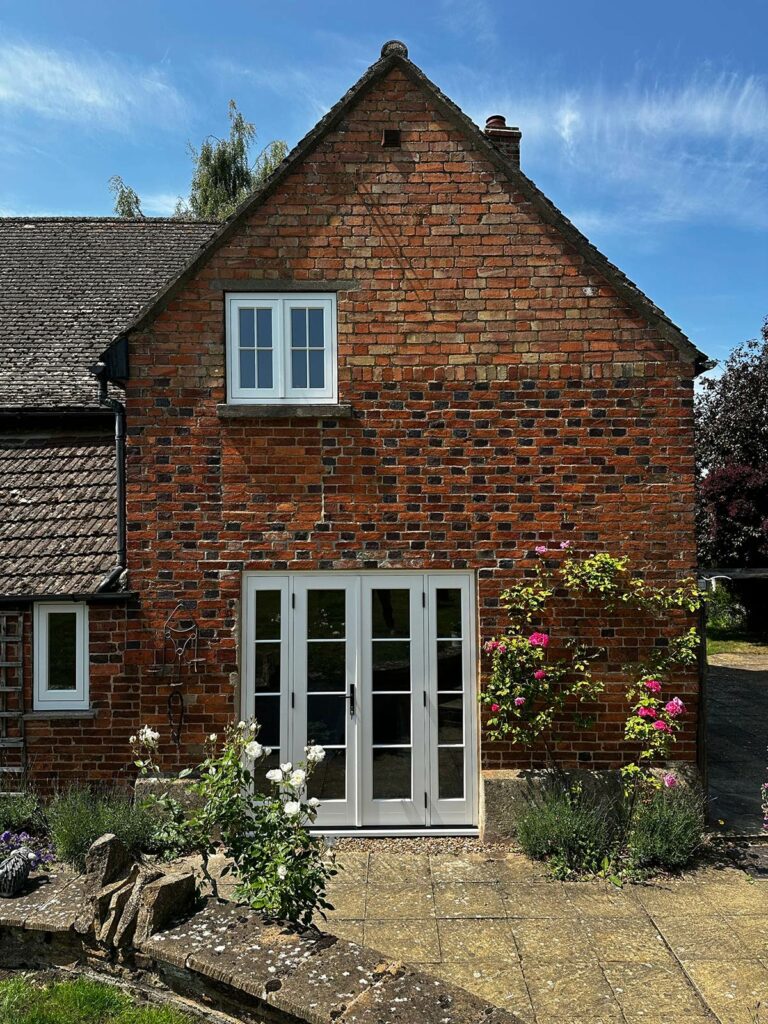 the back of a red brick home with white windows and doors