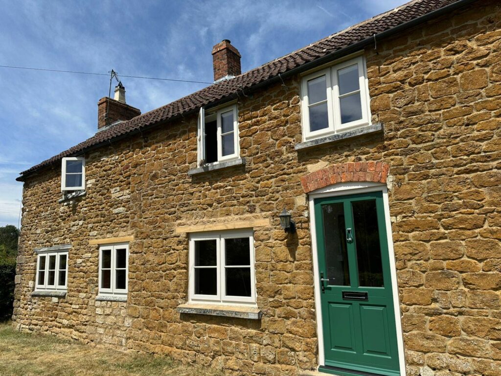 white windows and a green front door on a stone cottage