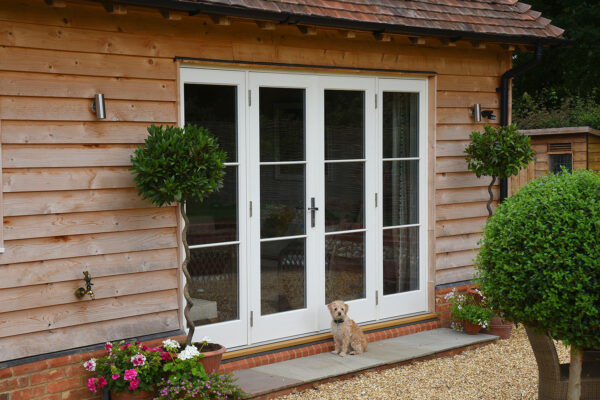 a white set of french doors with a dog sat in front, on a timber cladded building