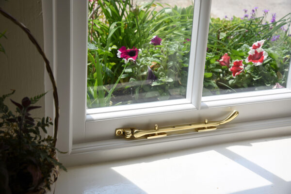 a brass window pegstay on a white window