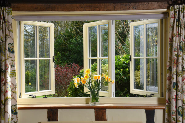 a set of open windows with daffodils in a vase on the window cill