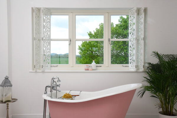 a pink bath in front of white casement windows