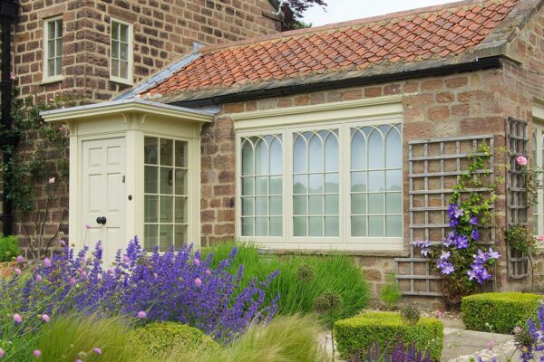 a yellow front door with gothic casement windows, both in front of lavender plants