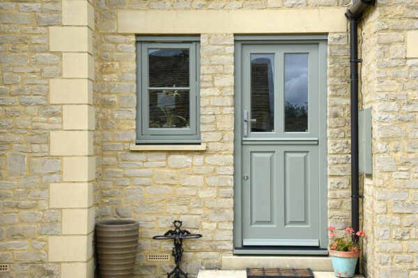 a green stable door and casement window on a cotswolds stone property