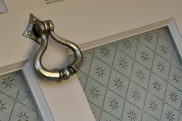 a pewter door knocker on a door with star patterned glass