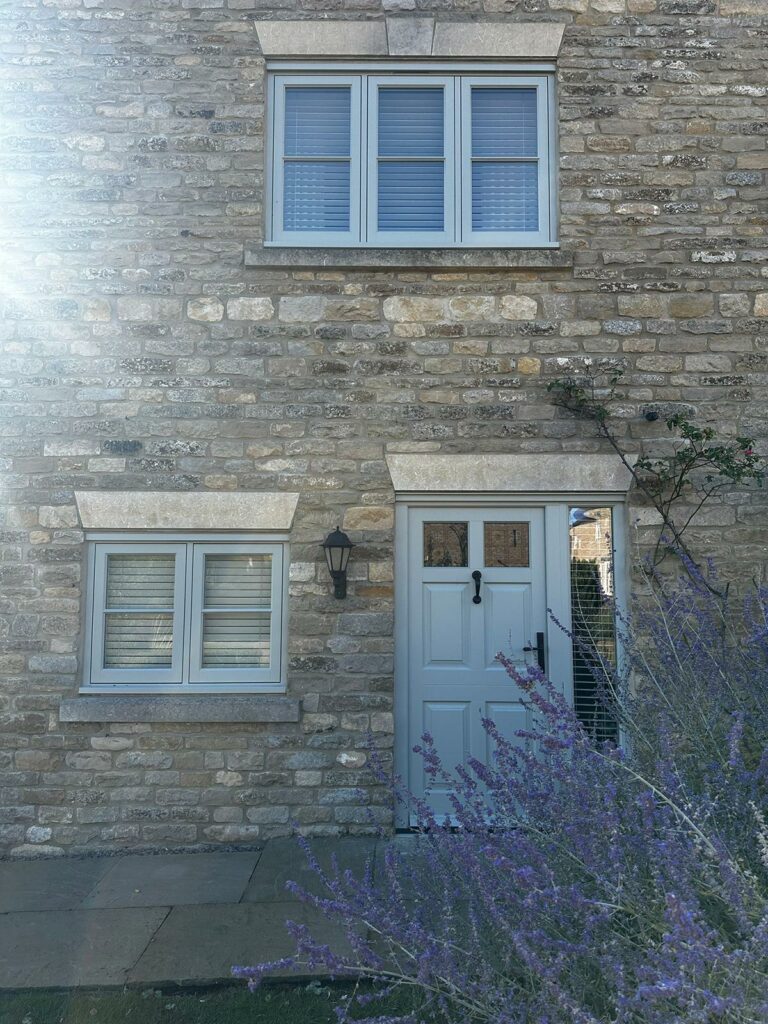 a front door alongside a set of flush casement windows, behind a lavender plant