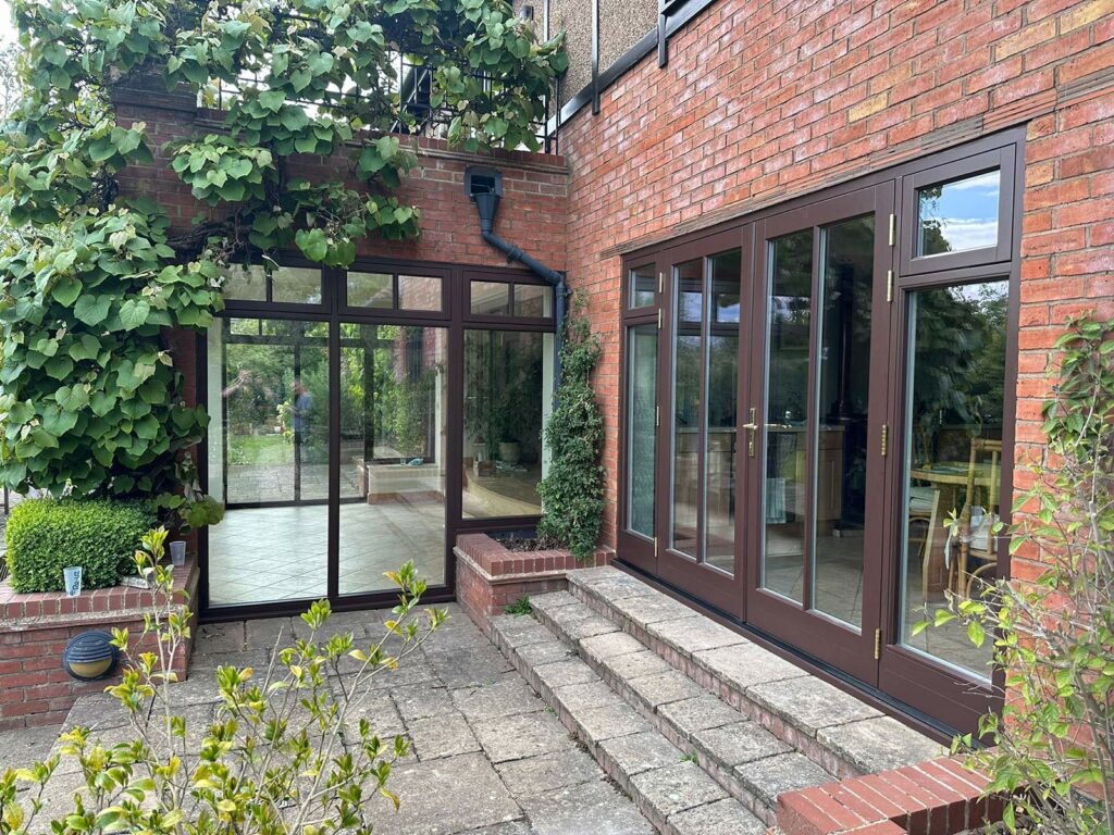 french doors and large fully glazed frames in a brown colour on a red brick home