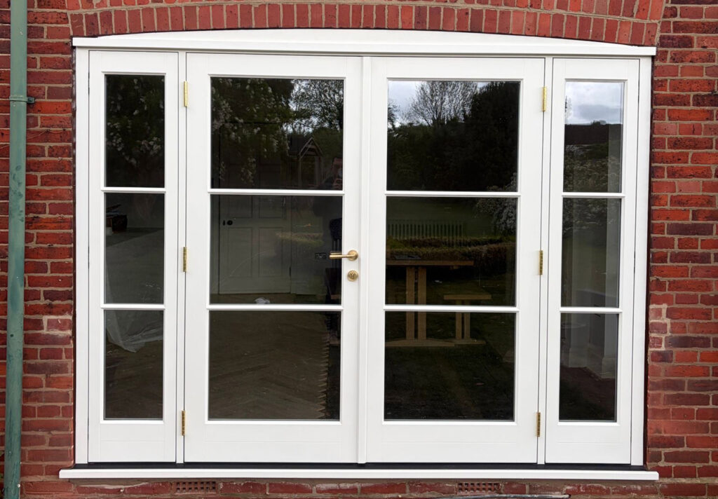 A white set of French doors with sidelights on a red brick house.