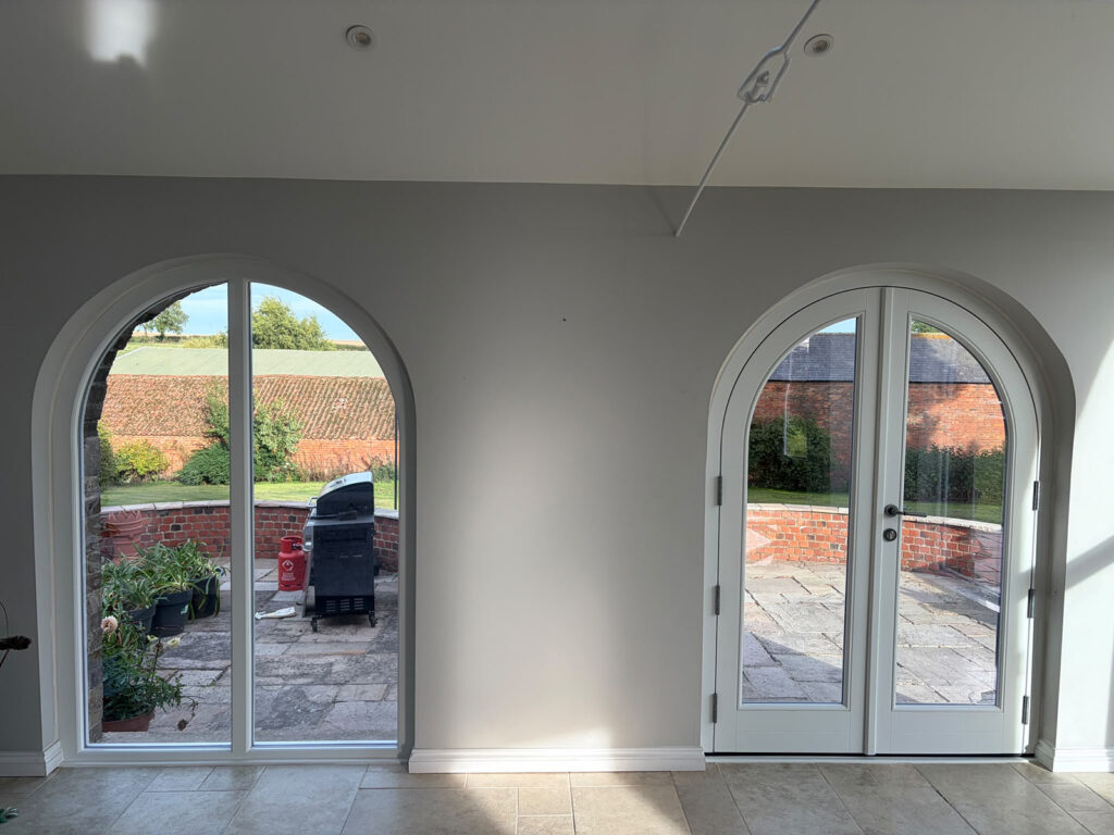 an empty white room with arched french doors and a large fixed frame