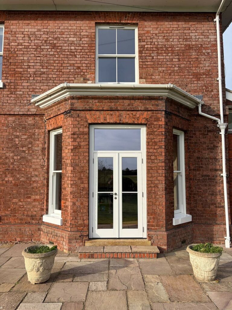 white french doors with a toplight on the rear of a large red brick home