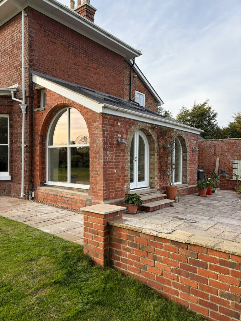 the side of a large red brick home with arched windows and french doors