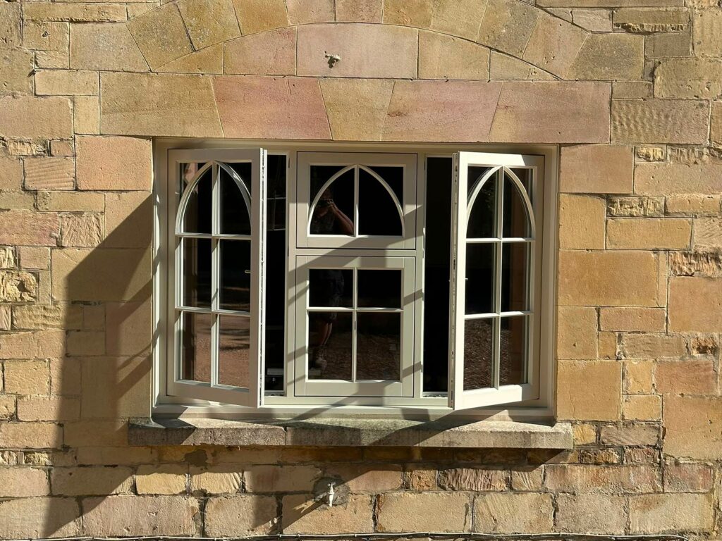 a casement window on a yellow stony property with gothic glazing bars